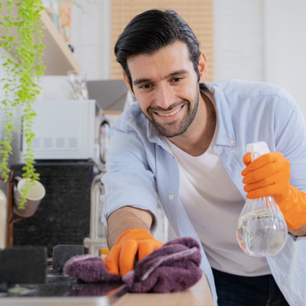 Clean your cares away. a young man disinfecting a kitchen counter at home. Young handsome man with apron and protective gloves wiping sink and faucet in kitchen.